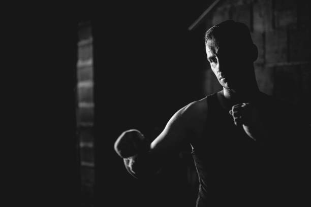 black and white picture of a man shadowboxing boxing in the dark throwing punches with hand wraps boxing training
