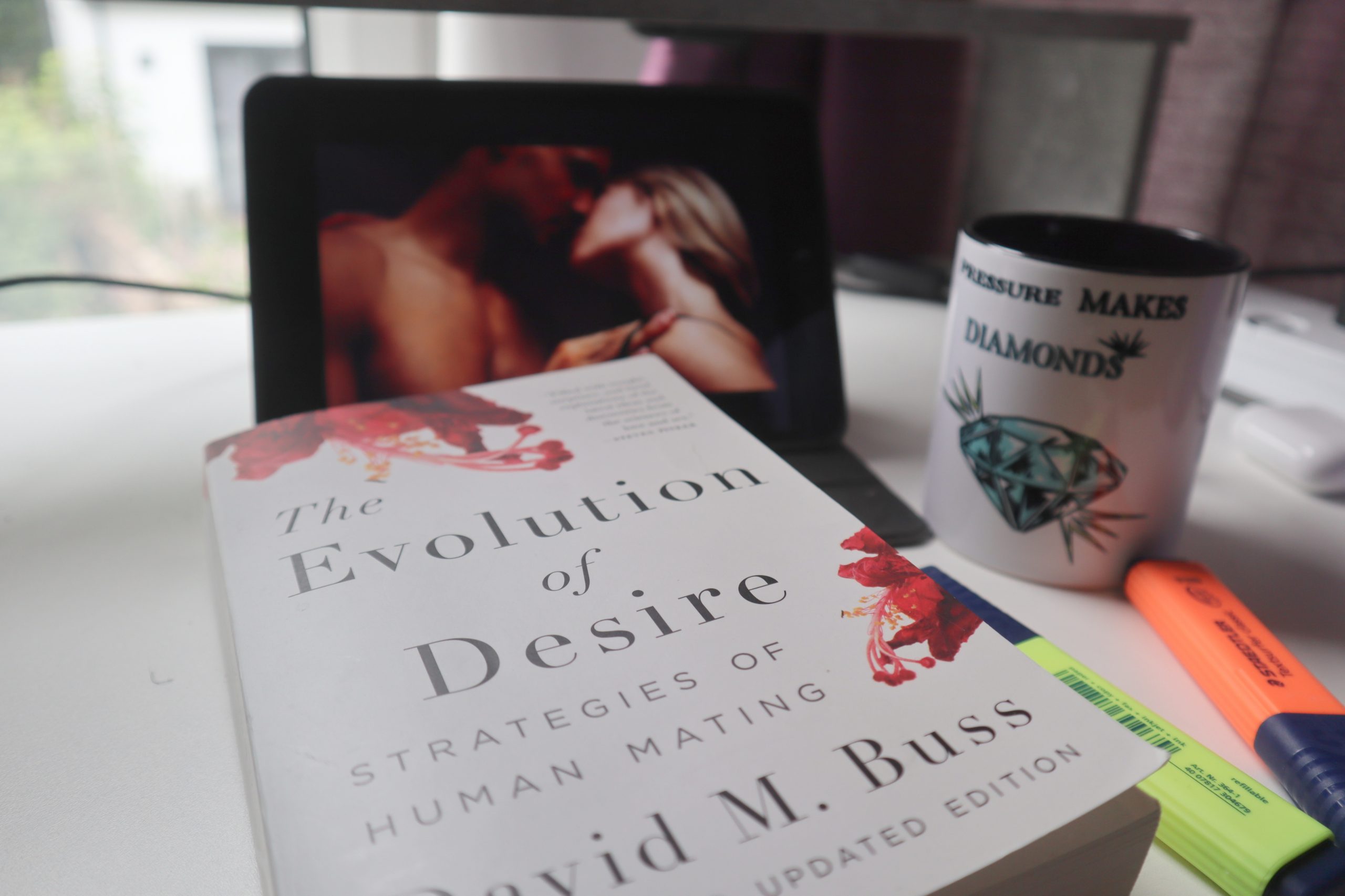 Desk reading Evolution of Desire: Strategies of Human Mating sexual pyschology book by David Buss, the psychologist who specialises in dating, marriage and relationship research observation studies on a desk table and coffee cup/mug