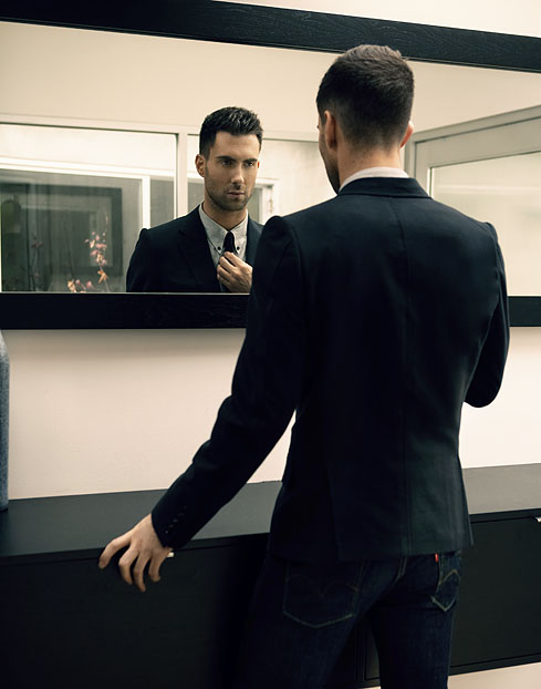Suave smart slick Man in black dark suit looking into his reflection in the mirror