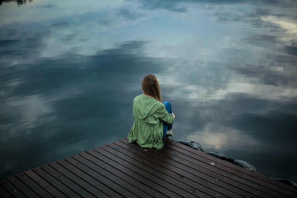 lonely woman sitting beside lake